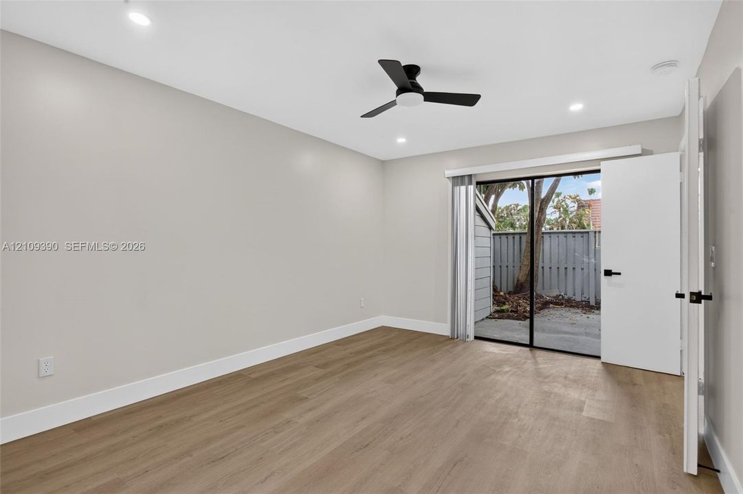 Neutral-toned interior featuring wood-finish flooring, recessed lighting, a matte black ceiling fan, and sliding glass doors with exterior access to a patio area