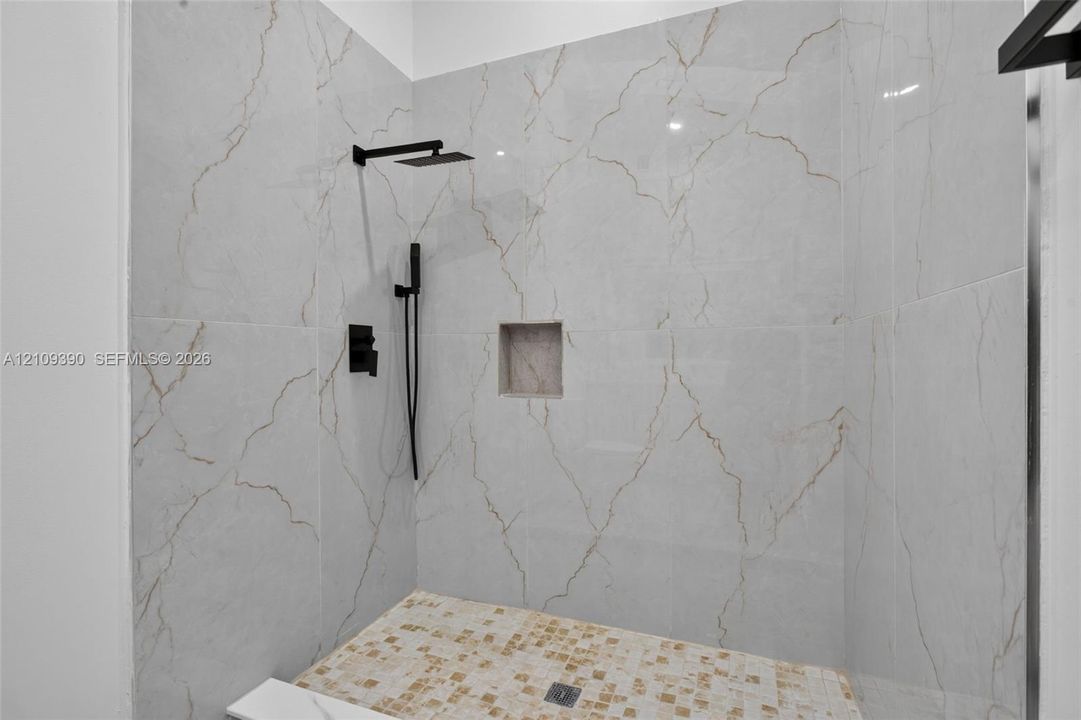 Walk-in shower featuring large-format stone-look wall tiling with veining detail, mosaic tile flooring, built-in recessed wall niche, and matte black rainfall showerhead with hand-held sprayer
