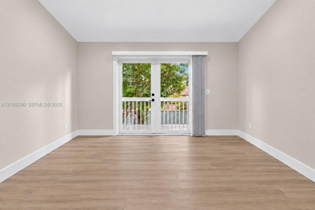 Neutral interior room featuring wood-finish flooring, white walls, and French doors opening to an exterior balcony