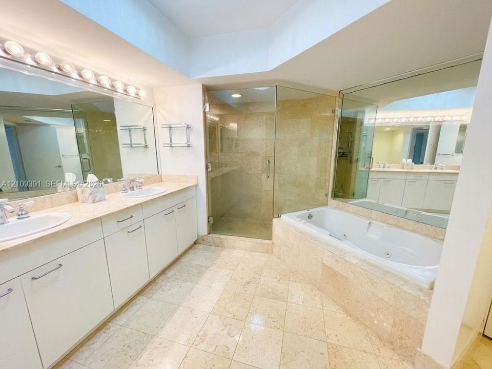 Dual-sink vanity with stone countertop, walk-in glass-enclosed shower, soaking tub with stone tile surround, stone flooring, and mirrored wall surfaces