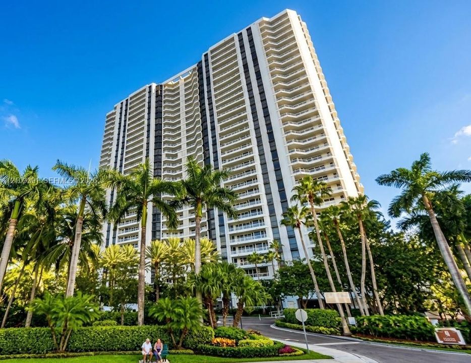 High-rise tower featuring multi-level private balconies, expansive glass windows, and a structured exterior facade, surrounded by established tropical landscaping
