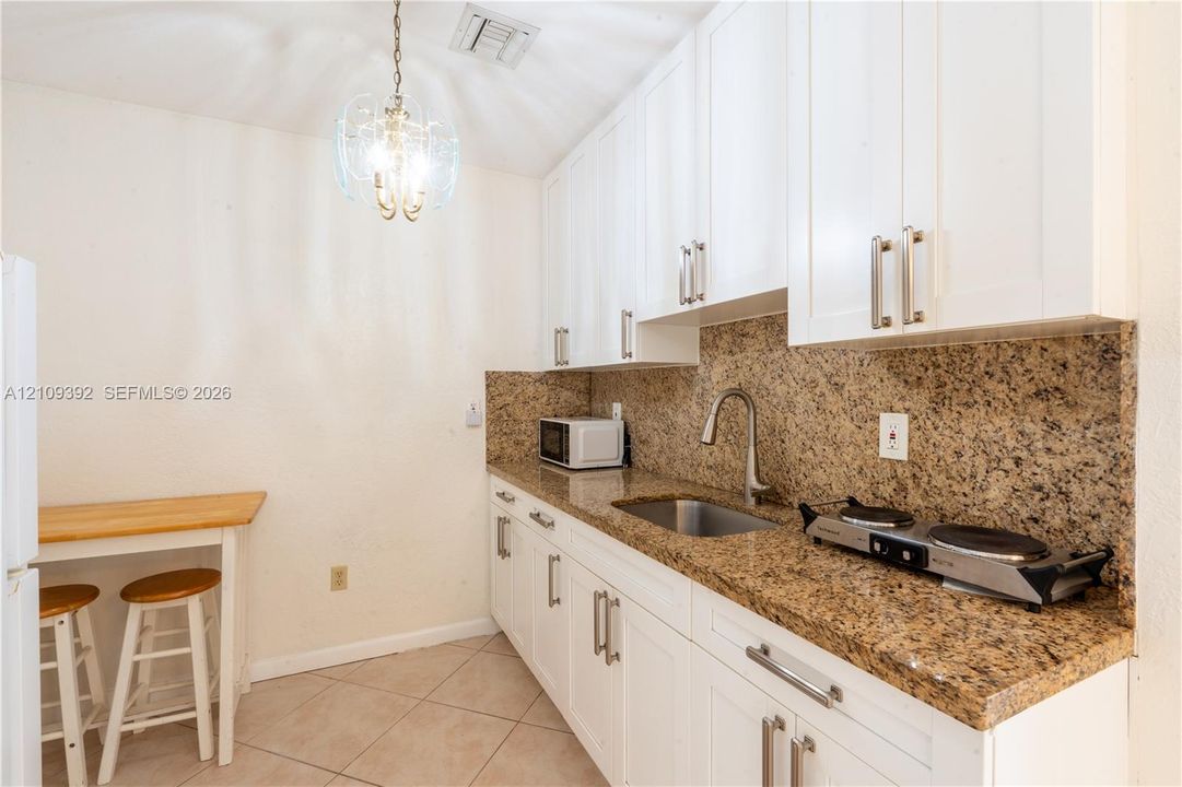 Kitchen featuring white cabinetry, stone-surface countertops, tile flooring, an undermount stainless steel sink with a pull-down faucet, and a decorative pendant light fixture