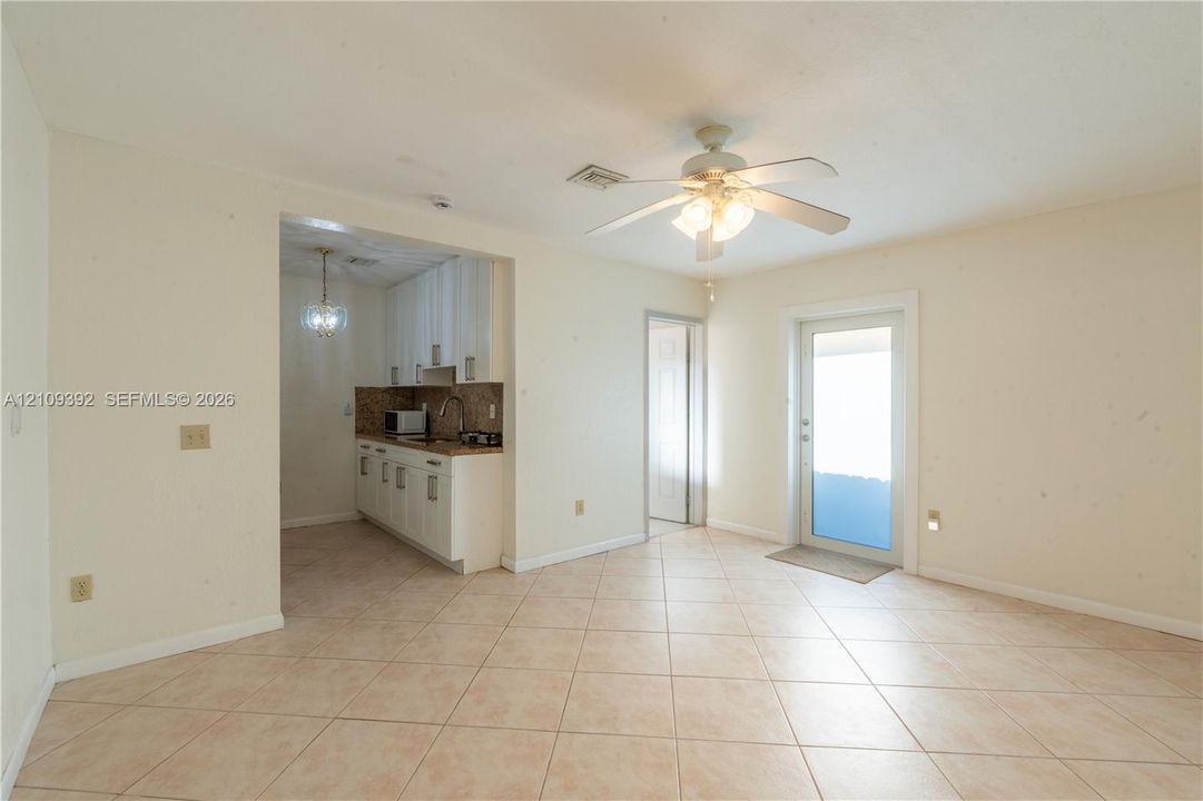 Tile flooring, ceiling-mounted light fixture with a fan, and white cabinetry featuring stone-surface countertops