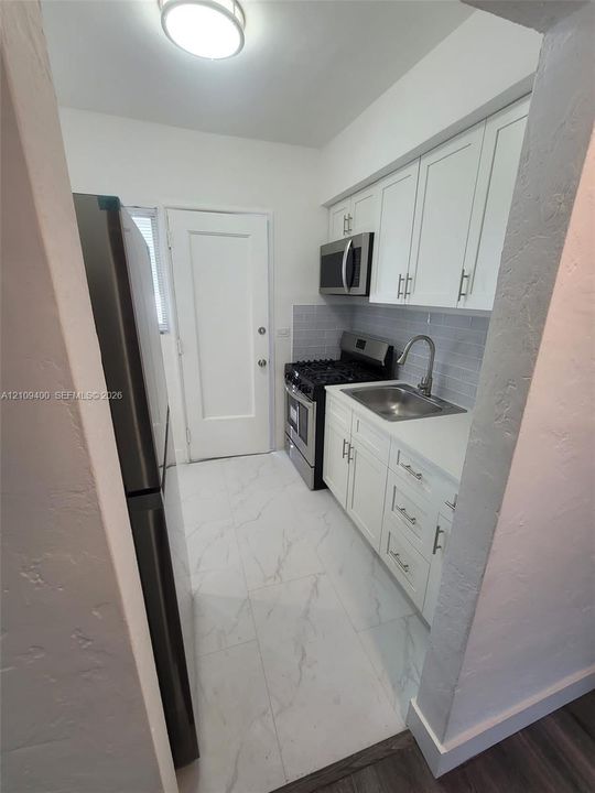 Kitchen featuring white shaker-style cabinetry, stainless steel appliances, grey subway tile backsplash, and stone-finish flooring