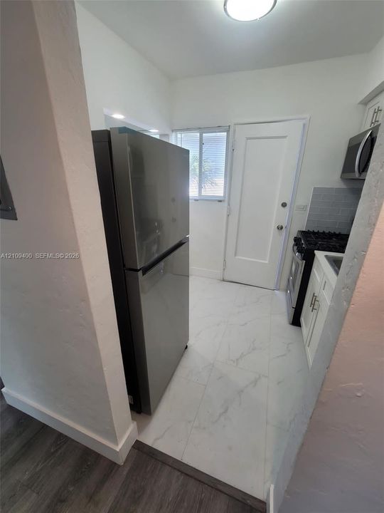 Kitchen featuring stone-finish floor tile, stainless steel refrigerator, white shaker-style cabinetry, and gas range