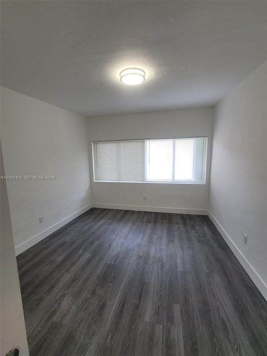 Room featuring wood-finish flooring, neutral walls, a multi-pane horizontal window, and a flush-mount overhead light fixture