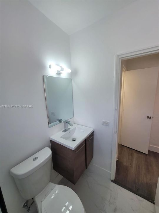 Floating vanity with wood-finish cabinetry, rectangular basin, chrome single-lever faucet, wall-mounted light fixture, and stone-finish tile flooring