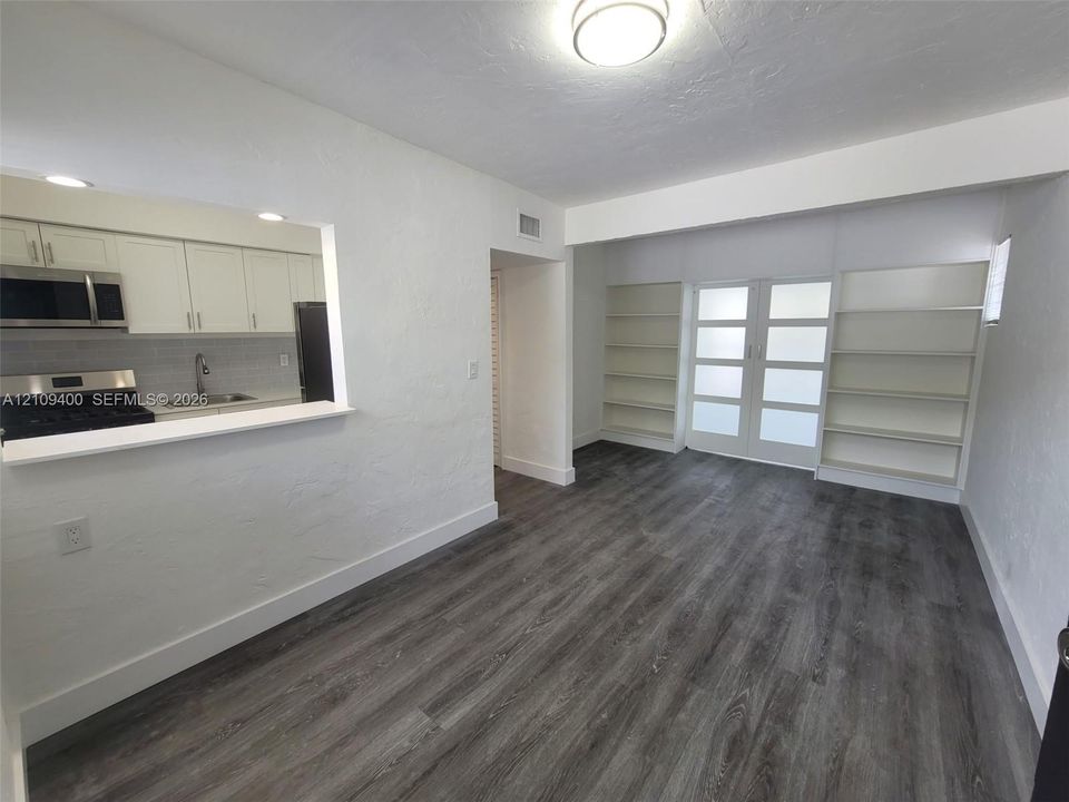 Kitchen featuring white cabinetry and stainless steel appliances, wood-finish flooring, dual built-in shelving units, and glass-paneled double doors