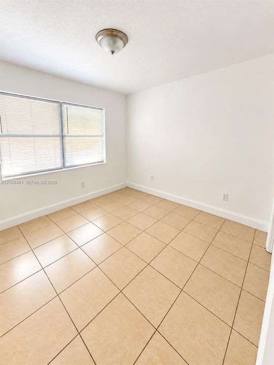 Neutral-toned ceramic tile flooring, crisp white wall finishes, and a flush-mount ceiling light fixture with an integrated window featuring horizontal blinds