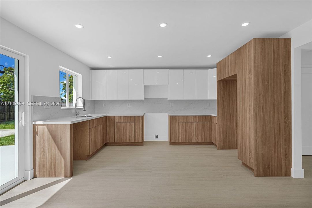 Kitchen featuring two-tone cabinetry, wood-finish lower cabinets, high-gloss white upper cabinets, stone-surfaced countertops, and recessed lighting