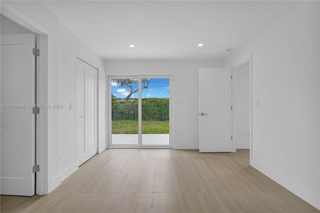 Interior space featuring wood-finish flooring, recessed lighting, white shaker-style interior doors, and sliding glass doors providing outdoor access