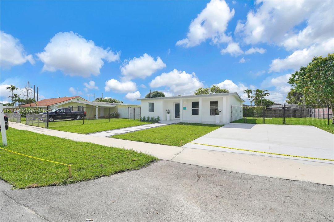 Single-story residence featuring a clean white exterior, recessed entry, concrete driveway, and chain-link perimeter fencing