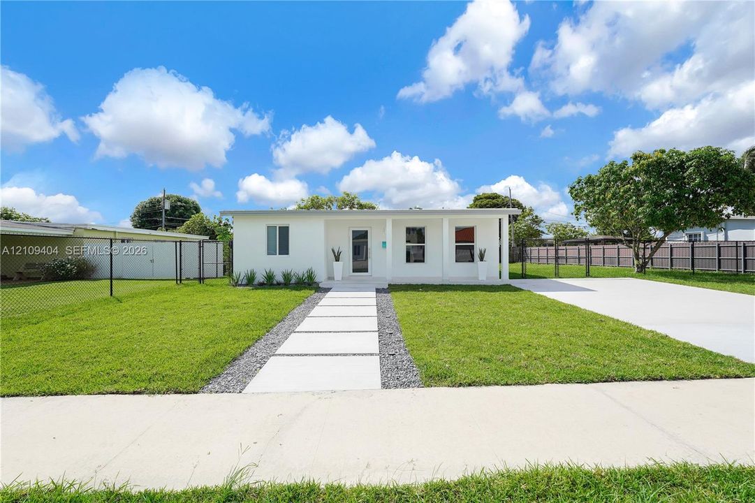 Single-story exterior featuring a covered front porch, concrete paver walkway, gravel landscaping, attached carport, and a concrete driveway