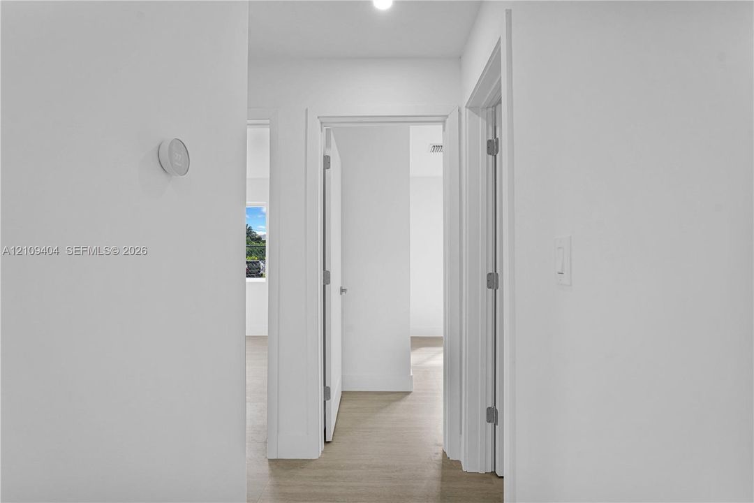 Neutral-toned interior featuring wood-finish flooring, white walls, recessed ceiling lighting, a mounted smart thermostat, and interior swinging doors