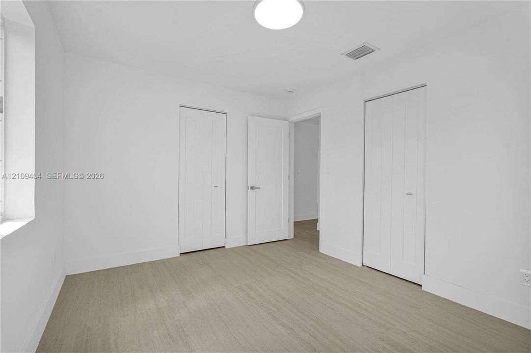 Neutral interior space featuring wood-finish flooring, crisp white wall finishes, two-panel interior doors, and dual bi-fold closet doors