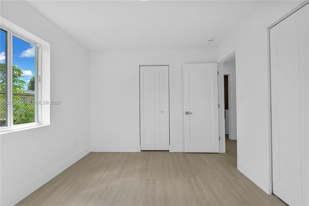 Neutral interior space featuring wood-finish flooring, crisp white walls, dual-panel interior doors, and a double-door closet