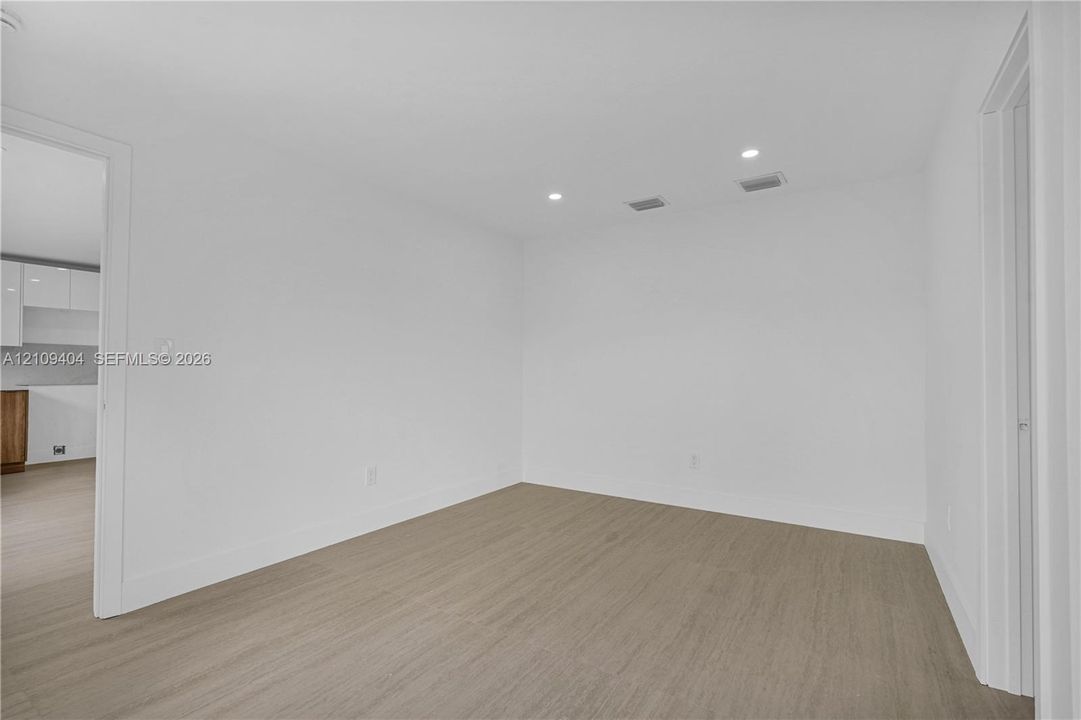 Neutral room featuring white walls, recessed ceiling lighting, and wood-finish flooring