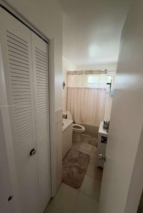 Bathroom featuring a louvered-door closet, tile flooring, wall-mounted vanity with a stone-top basin, and a tub-shower combination with tile surround