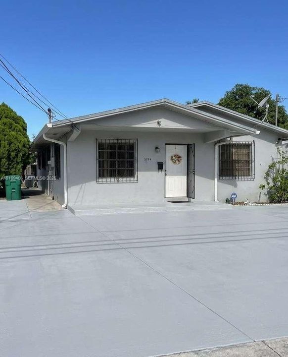 Single-story residence featuring a painted stucco exterior, gabled roofline, metal security window bars, and an expansive paved concrete driveway