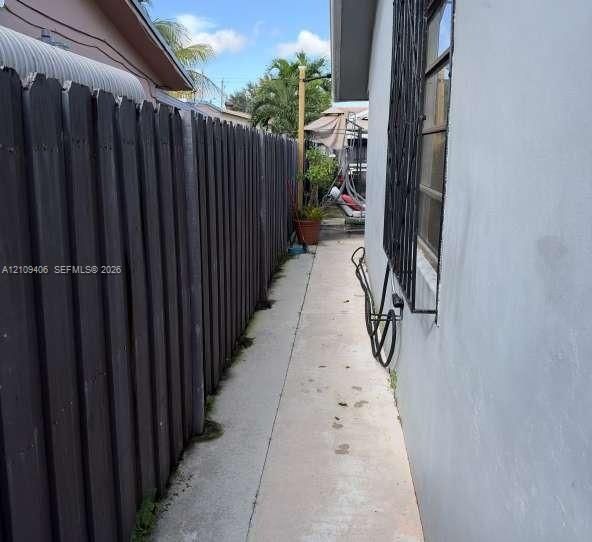 Concrete side yard walkway enclosed by a vertical wood-plank fence and exterior wall featuring metal security window bars