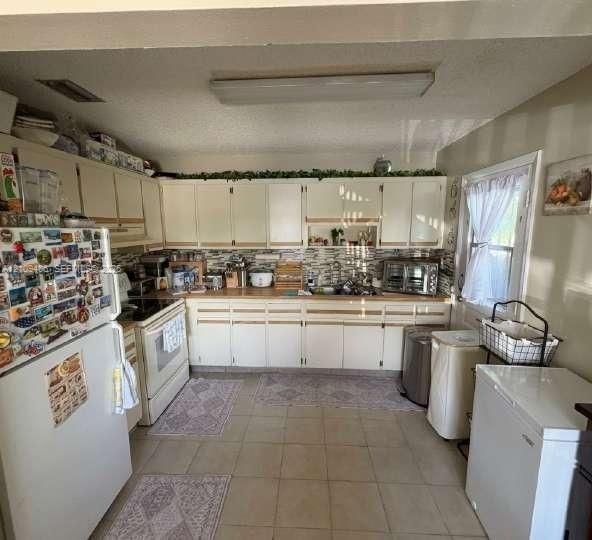Kitchen featuring white cabinetry, light-toned countertops, multi-tonal decorative tile backsplash, and tile flooring