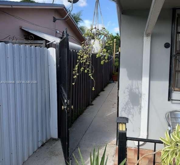 Concrete walkway bordered by a metal privacy fence and a metal swing gate, featuring a wall-mounted exterior light fixture