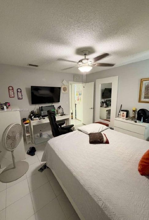 Neutral-toned interior featuring large-format tile flooring, a ceiling fan with integrated light fixture, and a full-length wall mirror