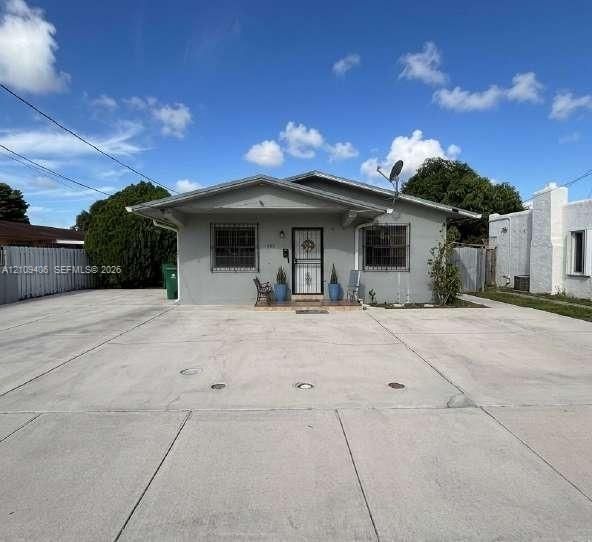 Single-story residence featuring a low-pitch roofline, an expansive concrete driveway, exterior window security bars, and a covered front entryway