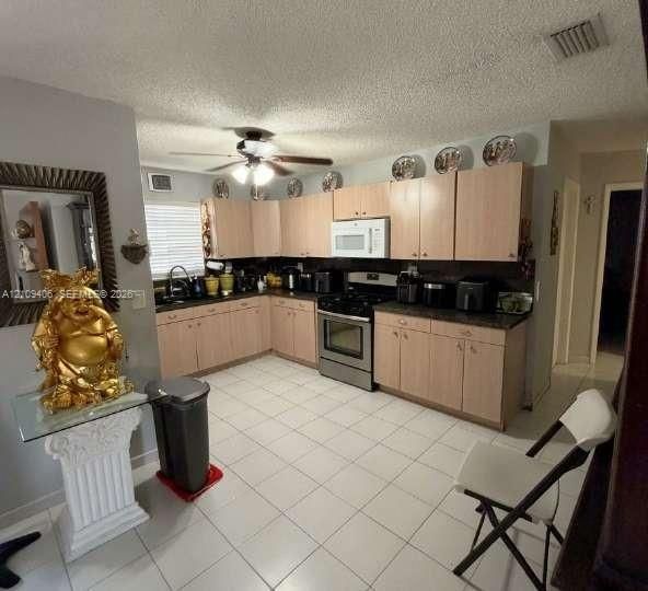 Kitchen featuring wood-finish cabinetry, dark solid-surface countertops, a stainless steel gas range, a built-in microwave, and ceramic tile flooring