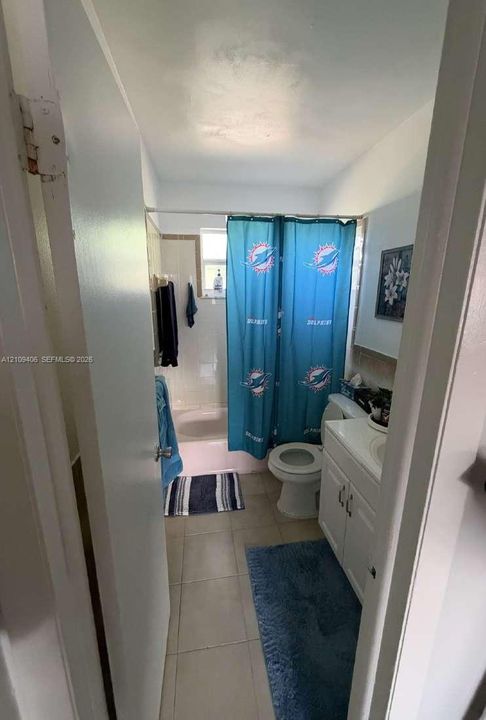 Bathroom featuring a white vanity cabinet with an integrated sink, ceramic tile flooring, and a shower-tub combination with light-toned wall tile surround