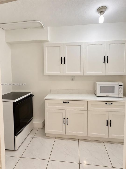 White cabinetry with matte black hardware, quartz countertop, and white tile flooring