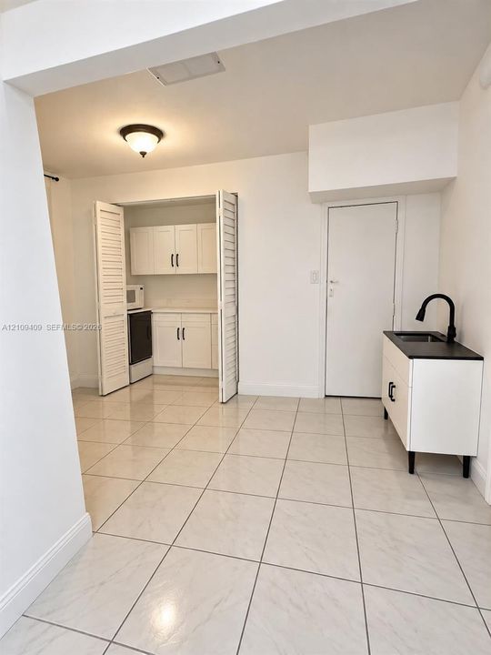 Tile flooring throughout, white cabinetry with matte black hardware, and a modern freestanding vanity with a contrasting countertop and matte black gooseneck faucet
