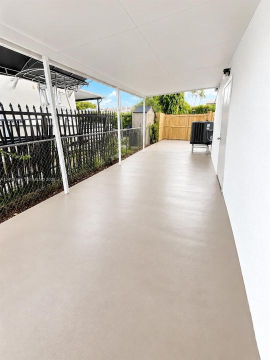 Covered outdoor patio with a concrete floor, chain-link perimeter fencing, and wood-panel enclosure