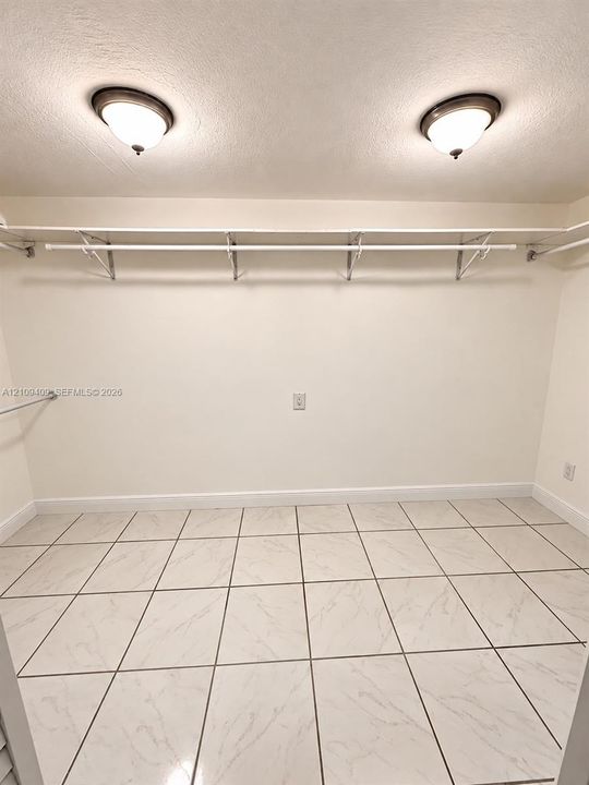 Walk-in closet featuring large-format stone-finish tile flooring, integrated ceiling-mounted dome lighting, and built-in white shelving with hanging rods