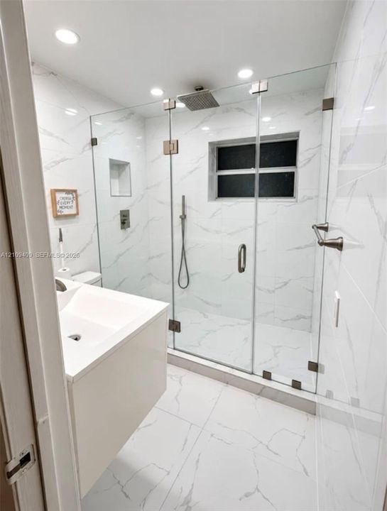 Walk-in shower featuring a frameless glass enclosure, rain-style showerhead, handheld sprayer, and recessed wall niche, complemented by large-format porcelain tile flooring and wall surfacing