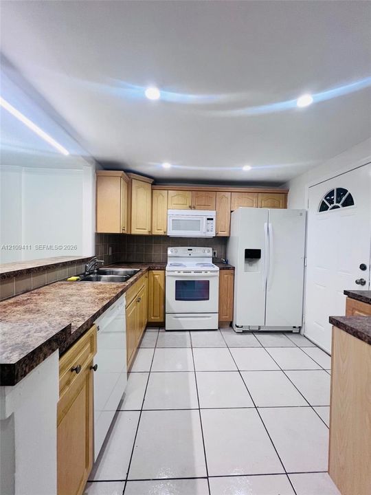 Kitchen featuring recessed ceiling lighting, wood-finish cabinetry, patterned laminate countertops, stainless steel dual-basin sink, and ceramic tile flooring