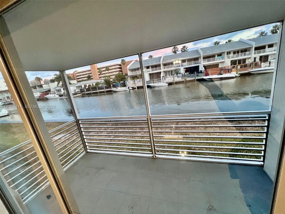 Covered balcony featuring tile flooring and horizontal metal railings overlooking a canal with bulkhead docks