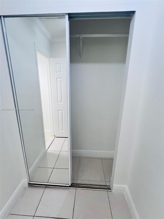 Sliding mirrored closet doors, large-format tile flooring, and a built-in garment rod