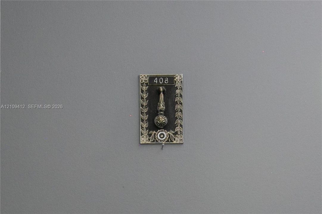 Decorative metal door knocker featuring an ornate floral border, engraved numbering, and a circular accent detail