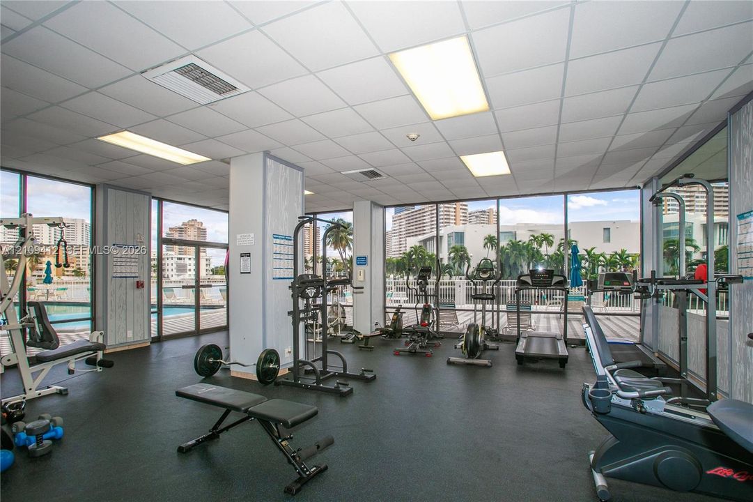 Fitness area featuring floor-to-ceiling windows, drop-tile ceiling with recessed lighting, and wall-to-wall rubberized flooring