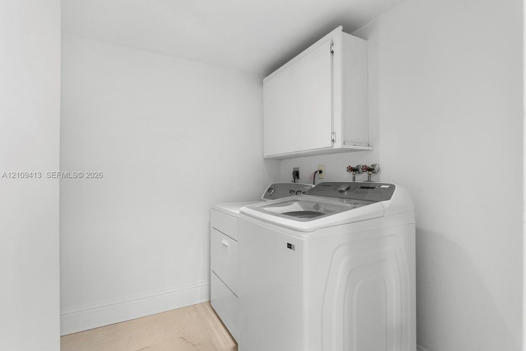 Dedicated laundry area featuring wall-mounted upper cabinetry and stone-finish flooring
