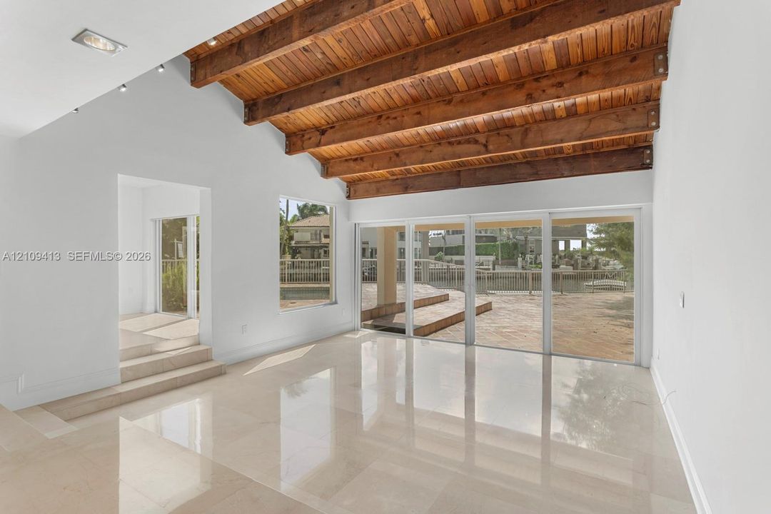 Vaulted ceiling featuring exposed wood beams, polished stone flooring, recessed lighting, and expansive floor-to-ceiling glass sliding doors