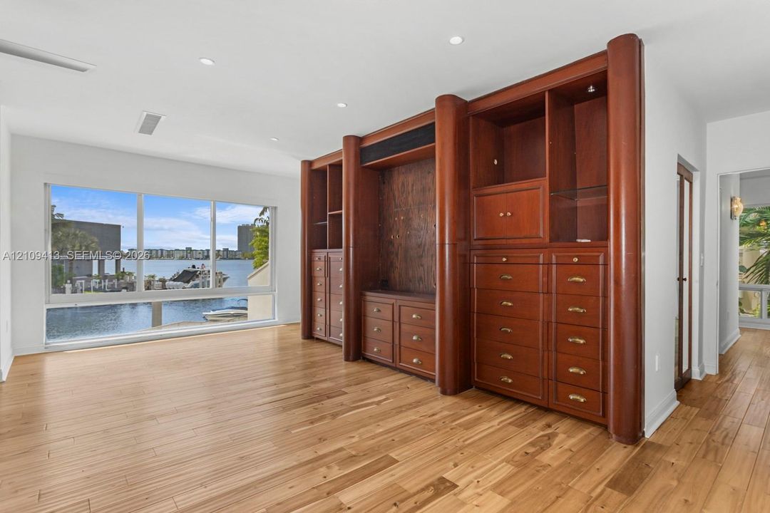Custom floor-to-ceiling wooden built-in cabinetry featuring drawers and shelving, wood-finish flooring, recessed lighting, and large picture windows