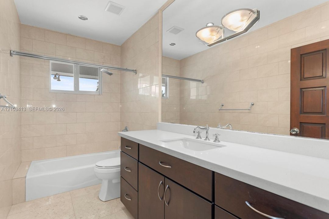 Bathroom featuring a stone-topped vanity with dark wood cabinetry, an integrated basin, a large wall-mounted mirror, and tile-surround bathtub