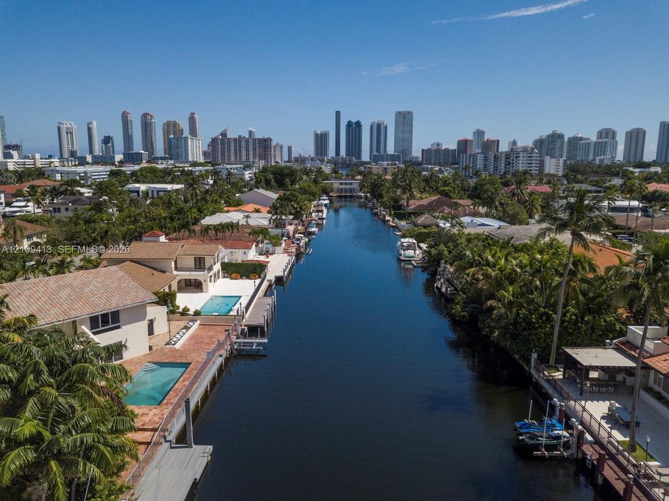Waterfront residential canal with direct bulkhead access, private boat docks, paved swimming pools, and prominent city skyline backdrop