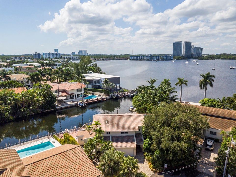 Waterfront property featuring a canal-side bulkhead, private swimming pool, terracotta-tiled roofs, and lush mature landscaping