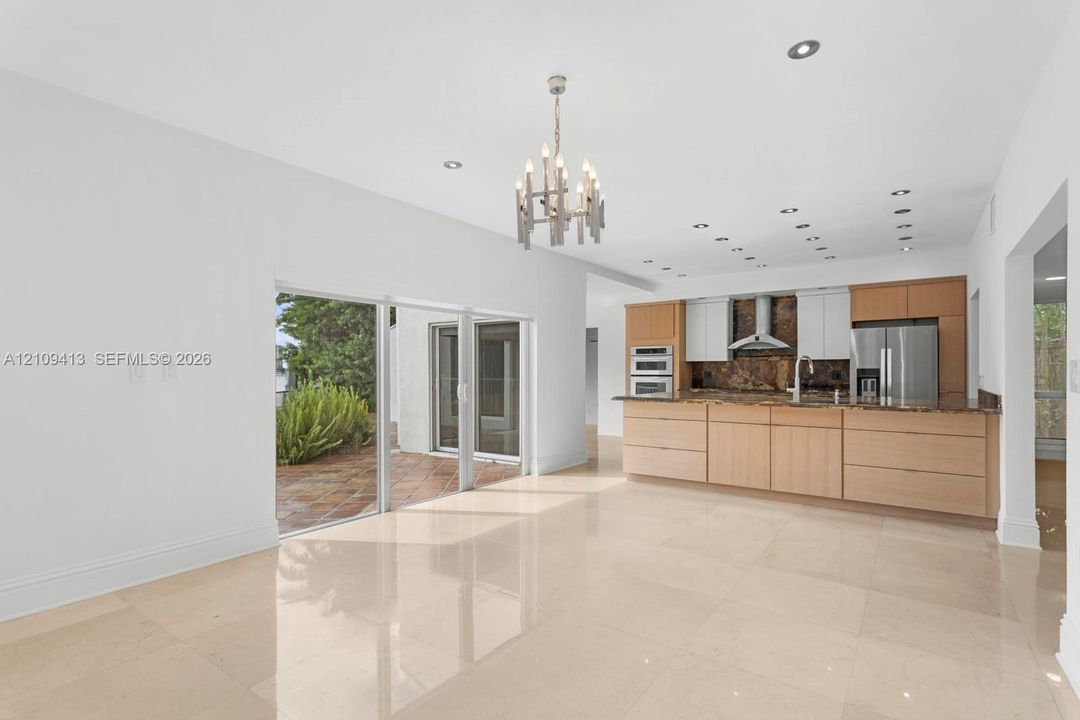 Open-concept interior featuring large-format tile flooring, recessed lighting, a modern multi-arm chandelier, wood-finish cabinetry, and glass sliding doors providing exterior access