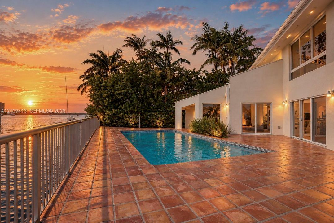 Waterfront patio featuring terracotta tile flooring, an in-ground swimming pool, metal perimeter railing, and exterior wall-mounted lighting