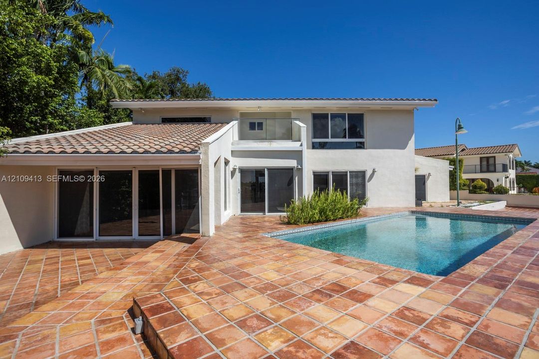 Stucco exterior featuring a tiled roof, expansive terra cotta patio, swimming pool with tiled coping, and multiple sliding glass door sets