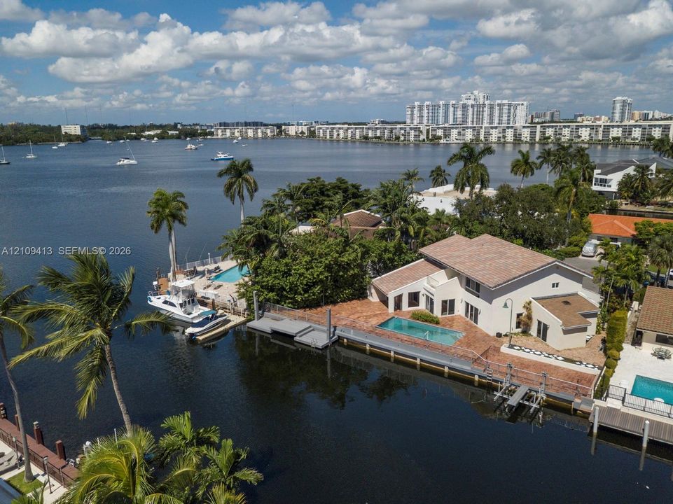 Waterfront property featuring a private boat dock, in-ground swimming pool, brick-paved patio, and mature palm trees